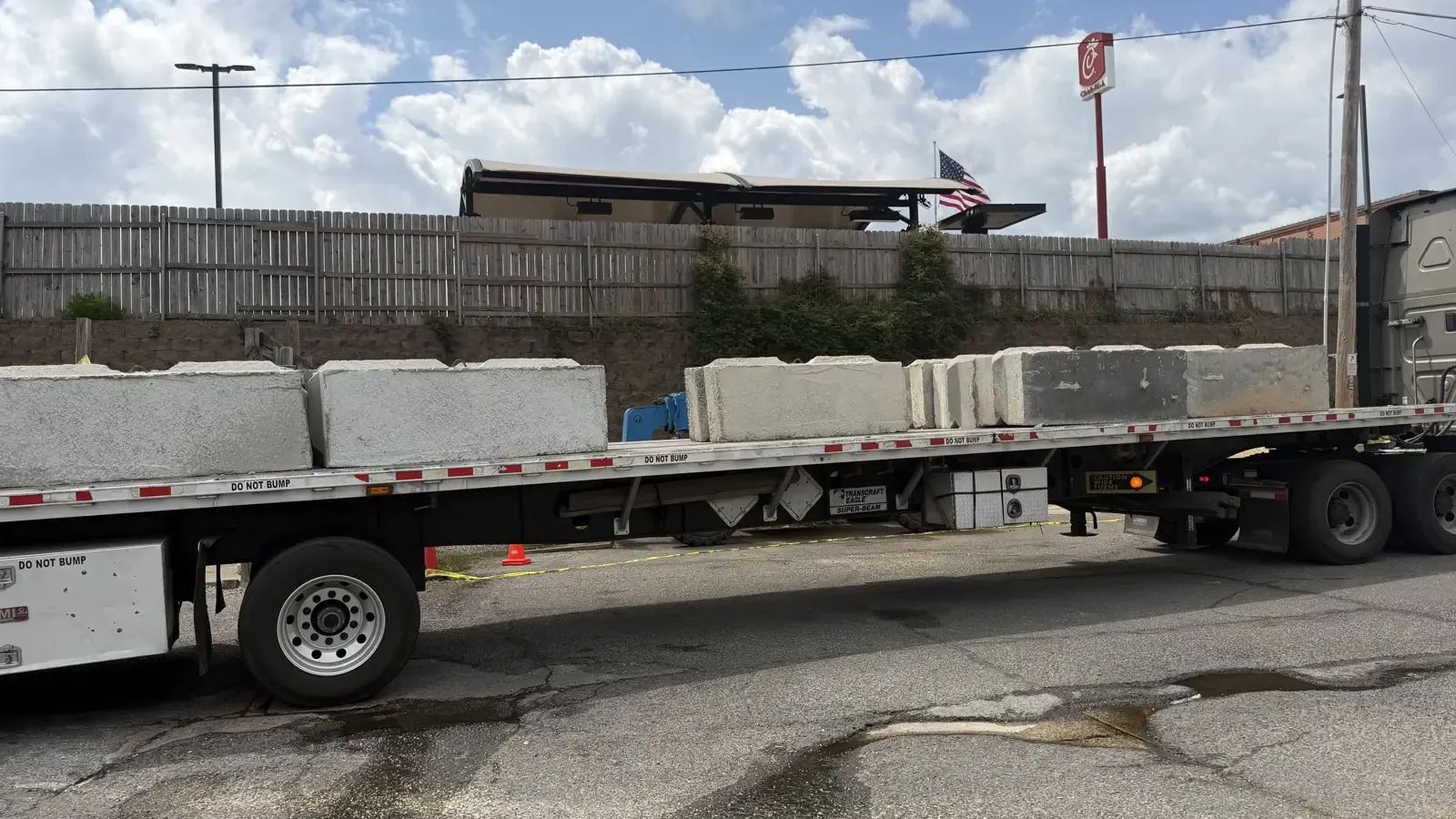 A flatbed trailer loaded with a single row of concrete barrier blocks, strapped down for the road