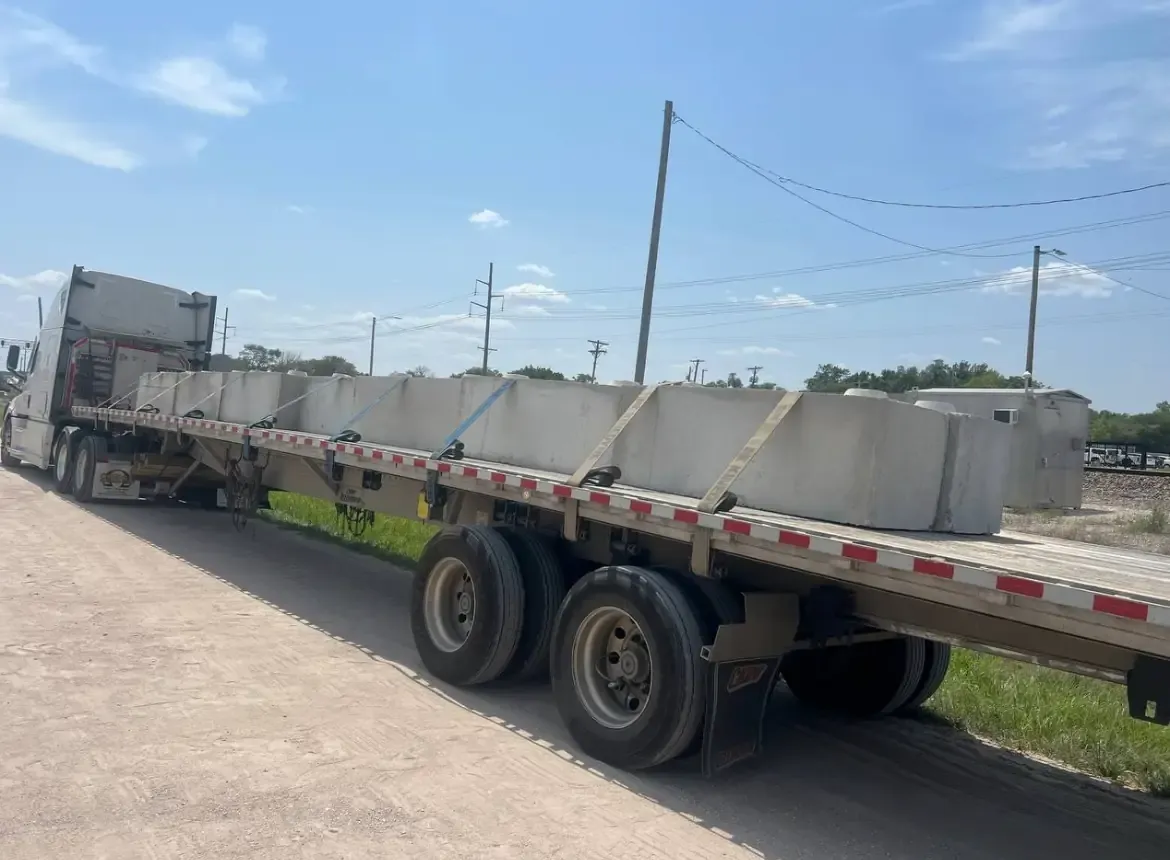 A tractor and flatbed loaded with concrete blocks waiting in an open lot